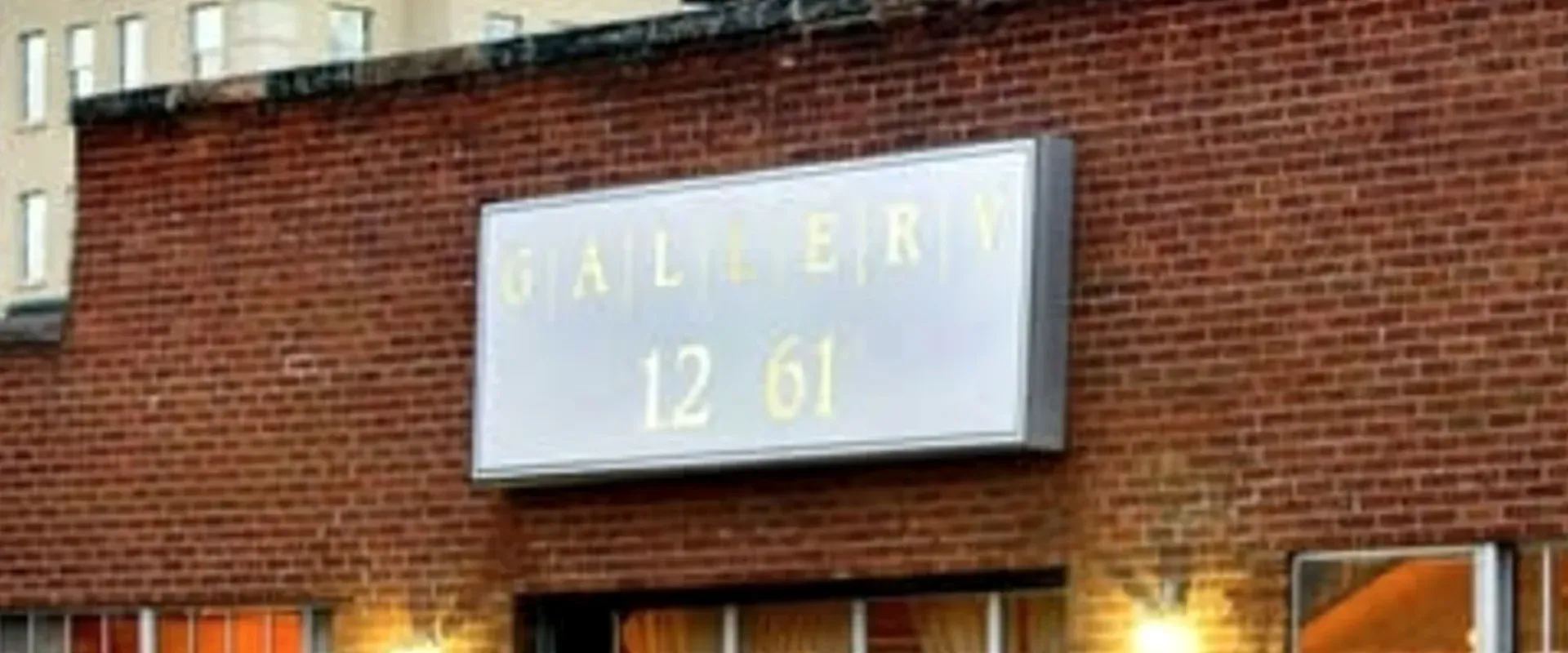 Red brick exterior wall of 1261 Delaware Street with the GALLERY 1261 sign at dusk.